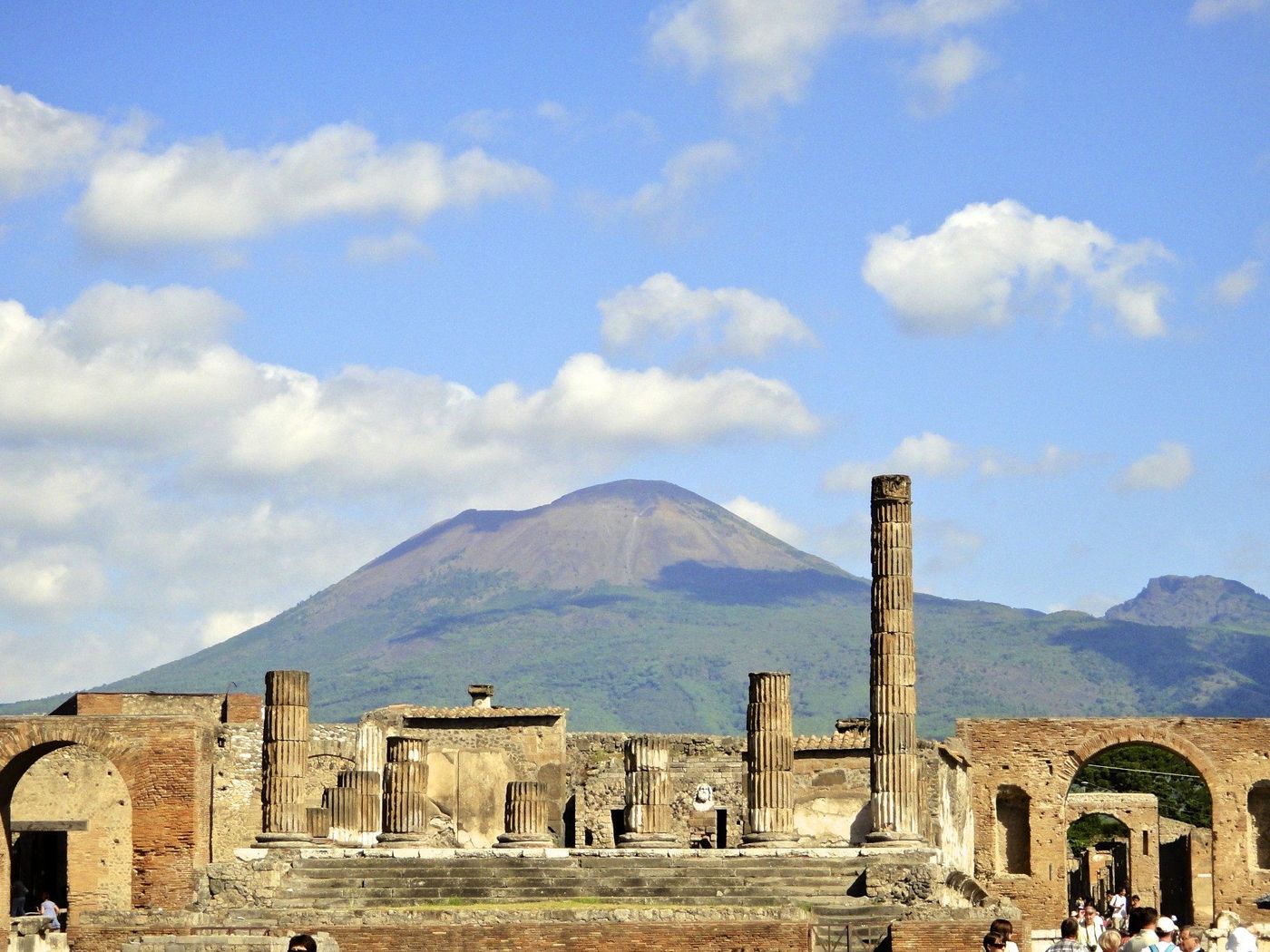 Roman ruins at Pompeii with a standing column and Mount Vesuvius behind